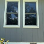 Two completed replacement windows on a gray-sided home